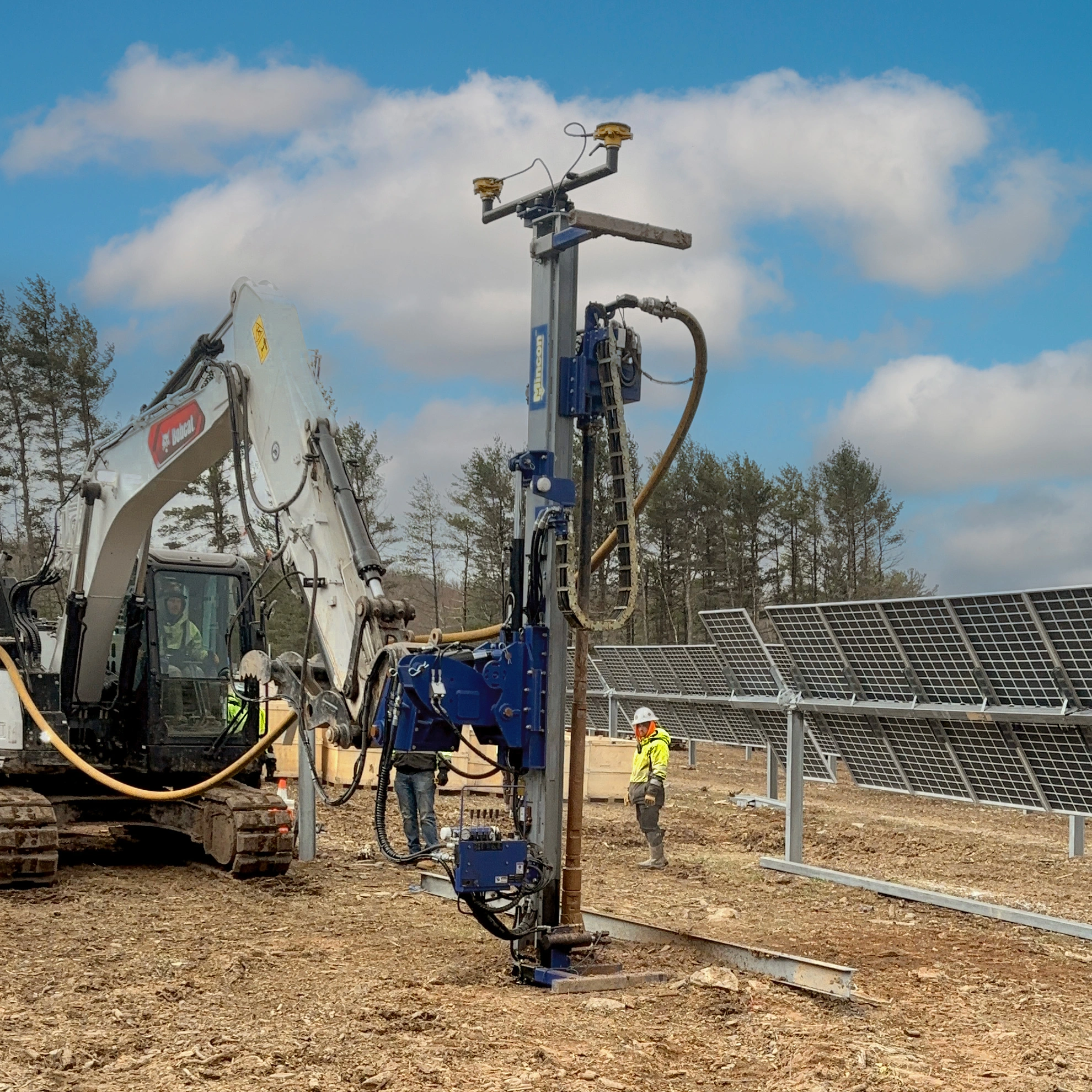 Mincon drill mast attachment mounted on a Bobcat excavator driving steel piles into the ground at a utility-scale solar farm construction site